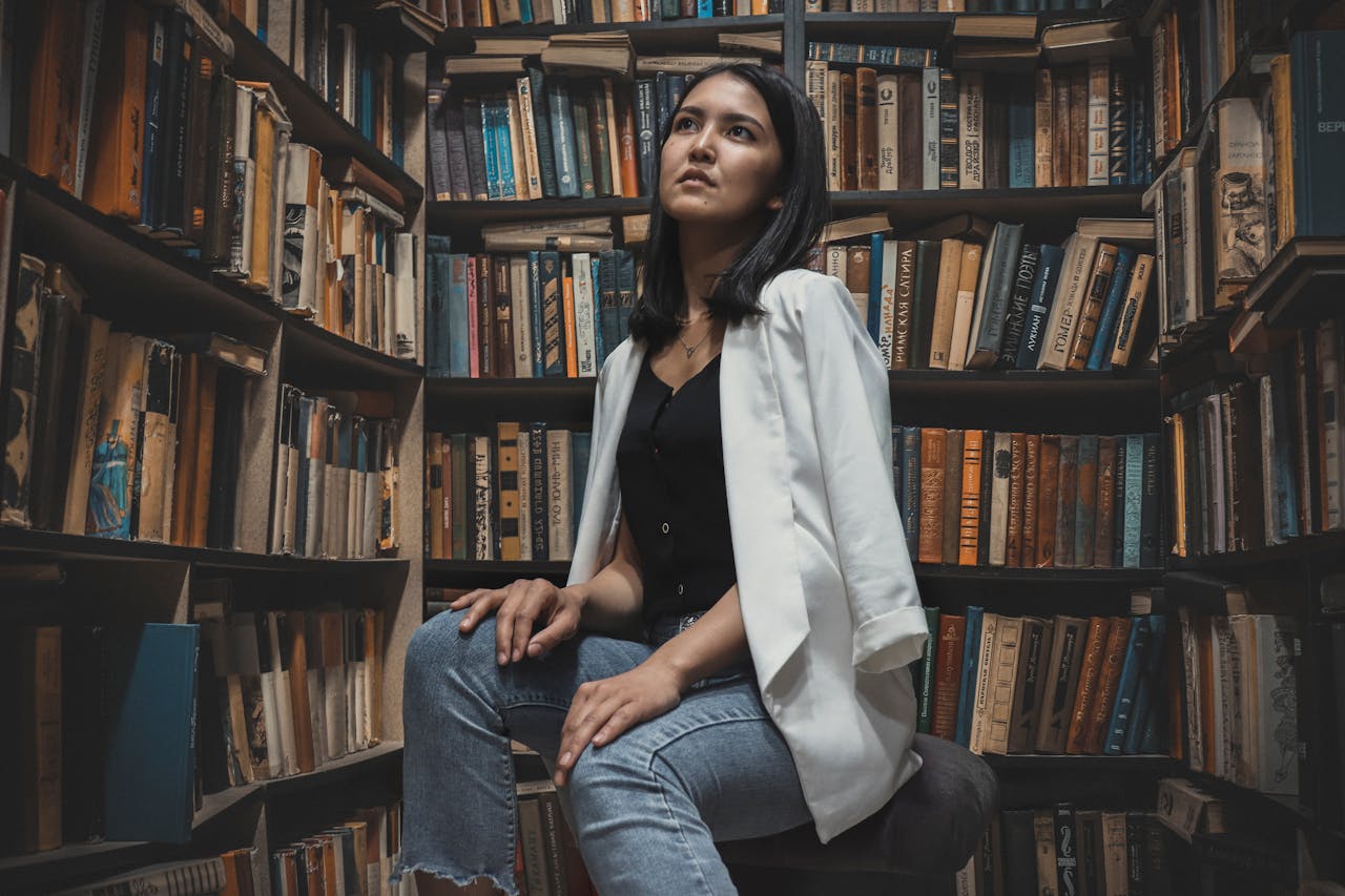 A young woman sits thoughtfully in a book-filled Kazakhstani library.