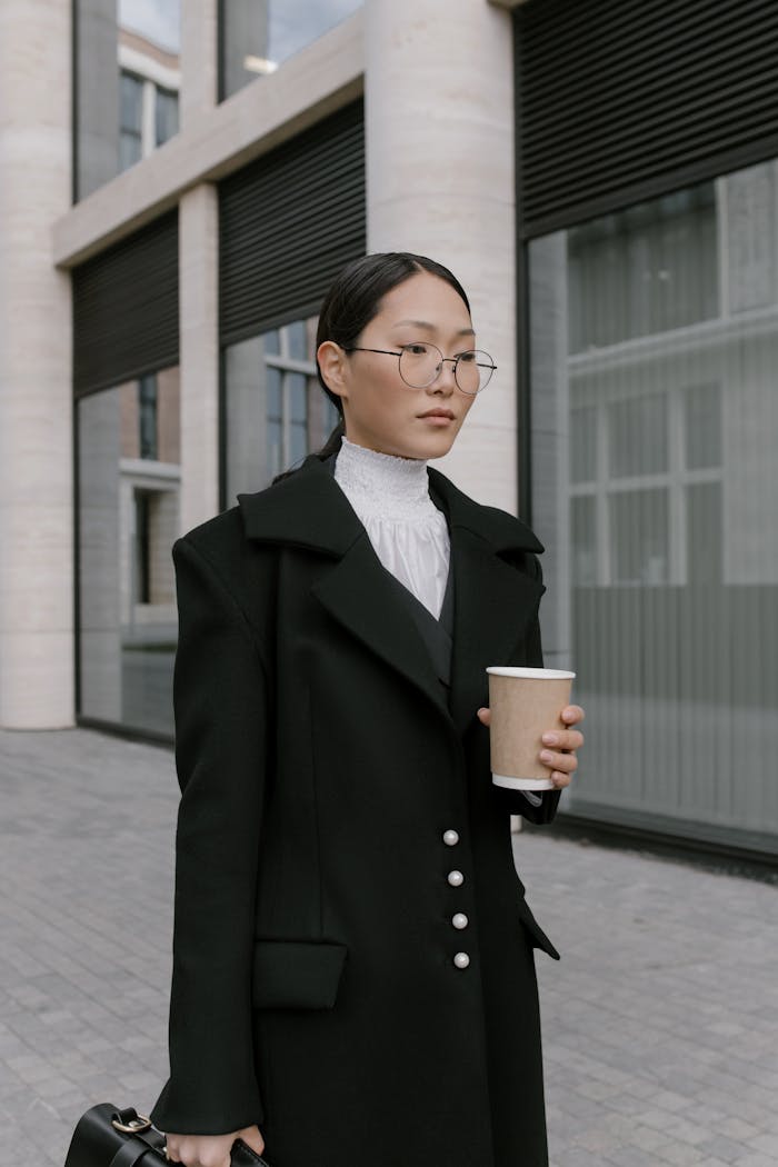 Confident businesswoman in black coat holding coffee cup outside modern building.